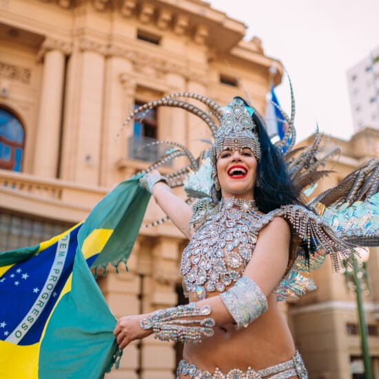 Beautiful Brazilian woman wearing colorful Carnival costume and Brazil flag during Carnaval street parade in city.